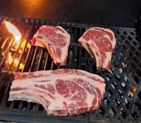 three steaks on a grill with a flame on them